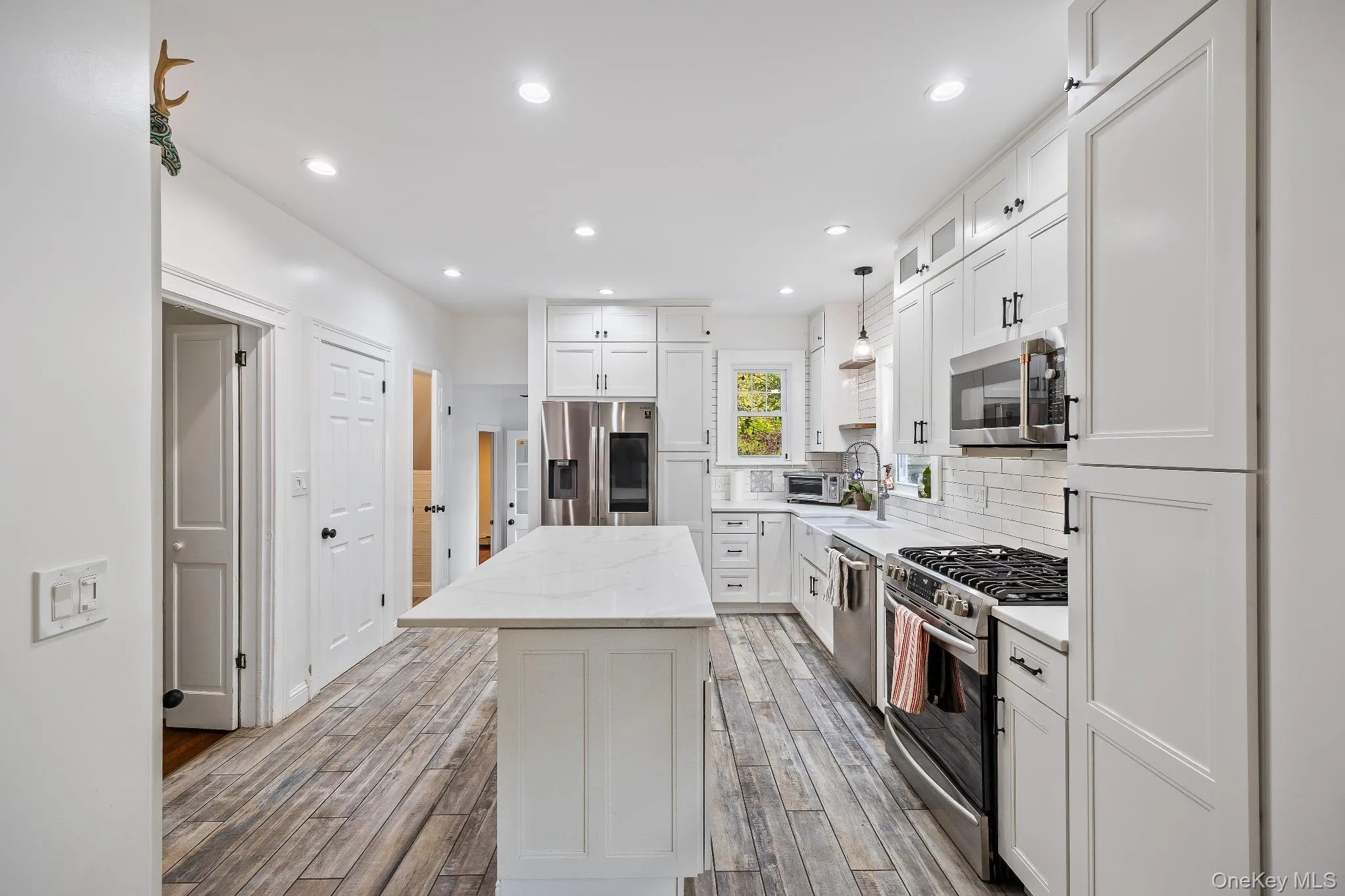 Kitchen with appliances with stainless steel finishes, white cabinets, a kitchen island, backsplash, and light stone counters Kitchen with appliances with stainless steel finishes, white cabinets, a kitchen island, backsplash, and light stone counters
