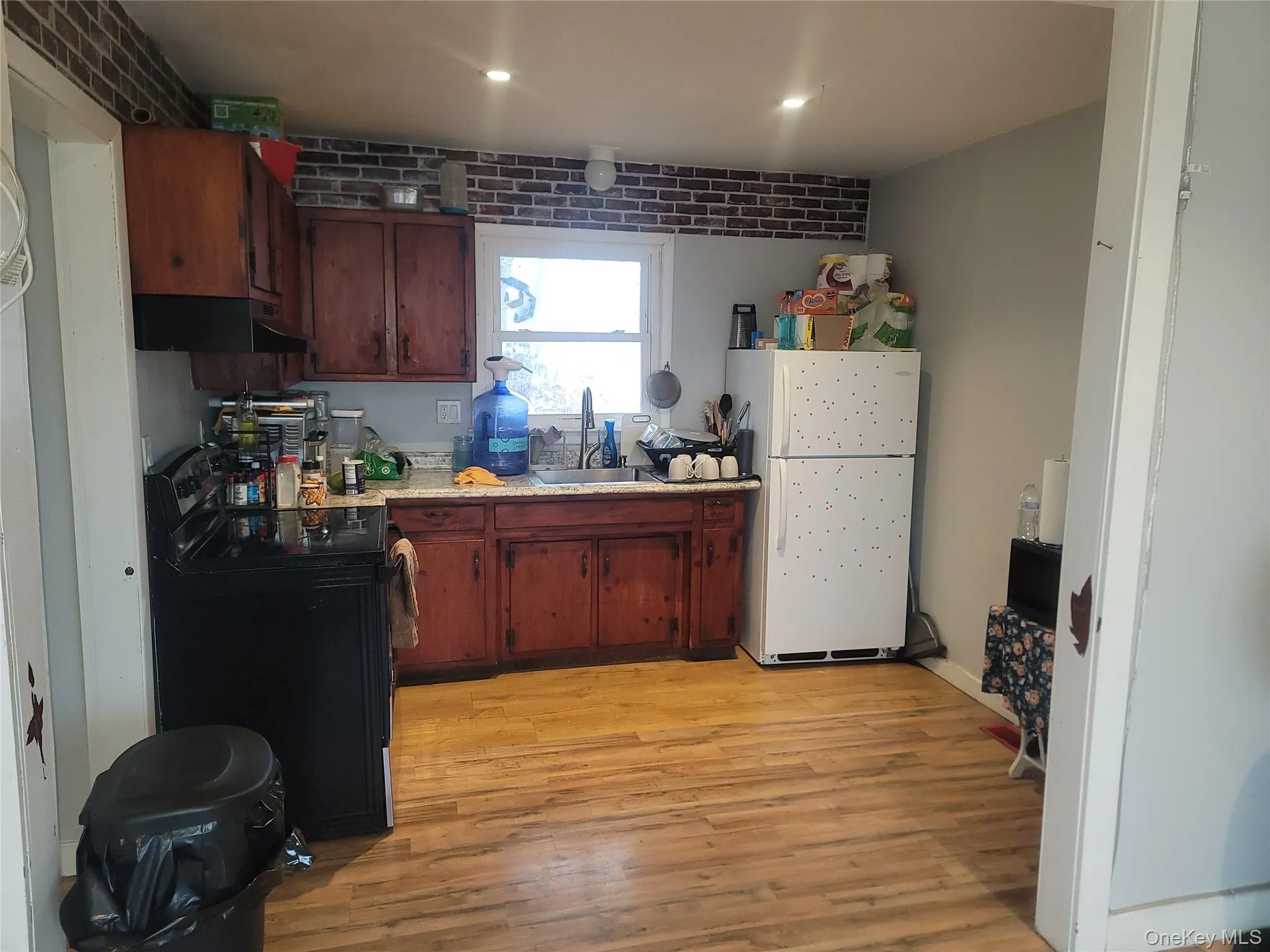 Kitchen featuring electric range, light countertops, freestanding refrigerator, light wood-type flooring, and brick wall Kitchen featuring electric range, light countertops, freestanding refrigerator, light wood-type flooring, and brick wall