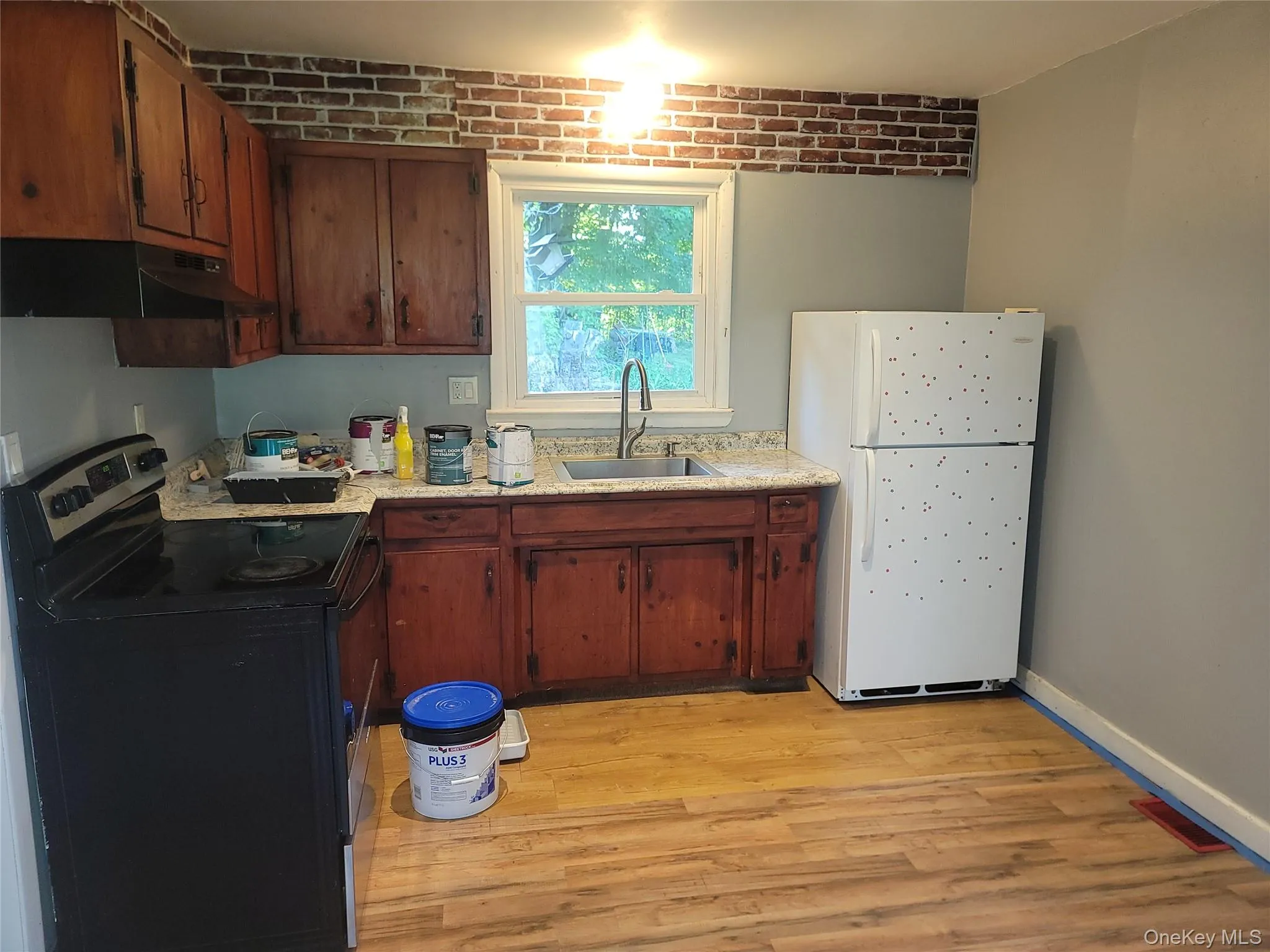 Kitchen featuring wood-finish flooring, wood cabinetry, a window above the sink, a range, and a refrigerator Kitchen featuring wood-finish flooring, wood cabinetry, a window above the sink, a range, and a refrigerator