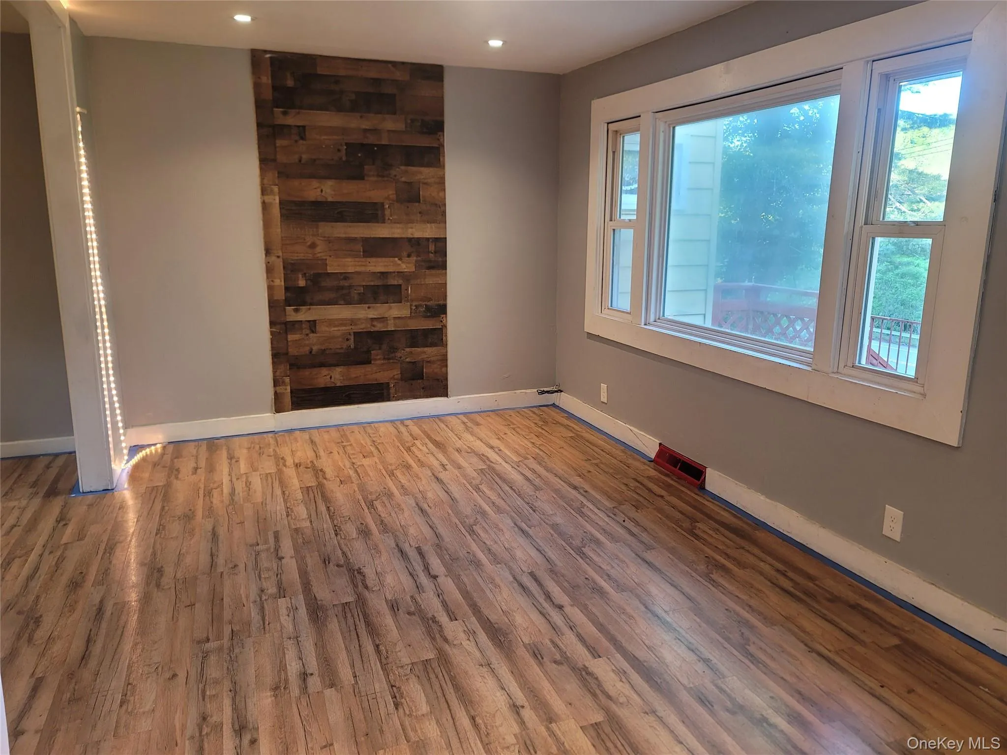 Spacious room featuring wood-finish flooring, a decorative wood plank accent wall, and recessed ceiling lighting Spacious room featuring wood-finish flooring, a decorative wood plank accent wall, and recessed ceiling lighting