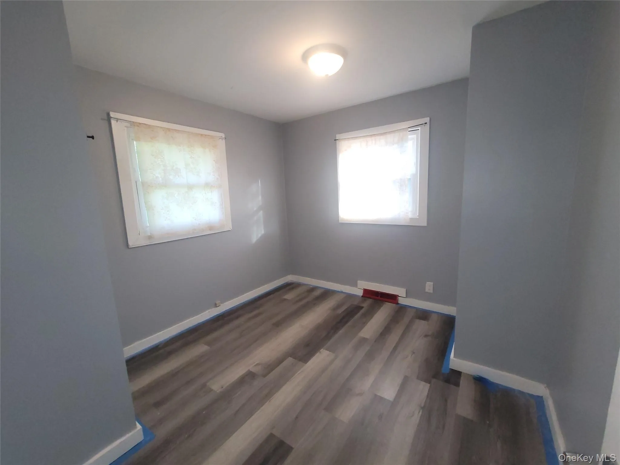 Room featuring wood-finish flooring, two windows, baseboard trim, and a ceiling-mounted light fixture Room featuring wood-finish flooring, two windows, baseboard trim, and a ceiling-mounted light fixture