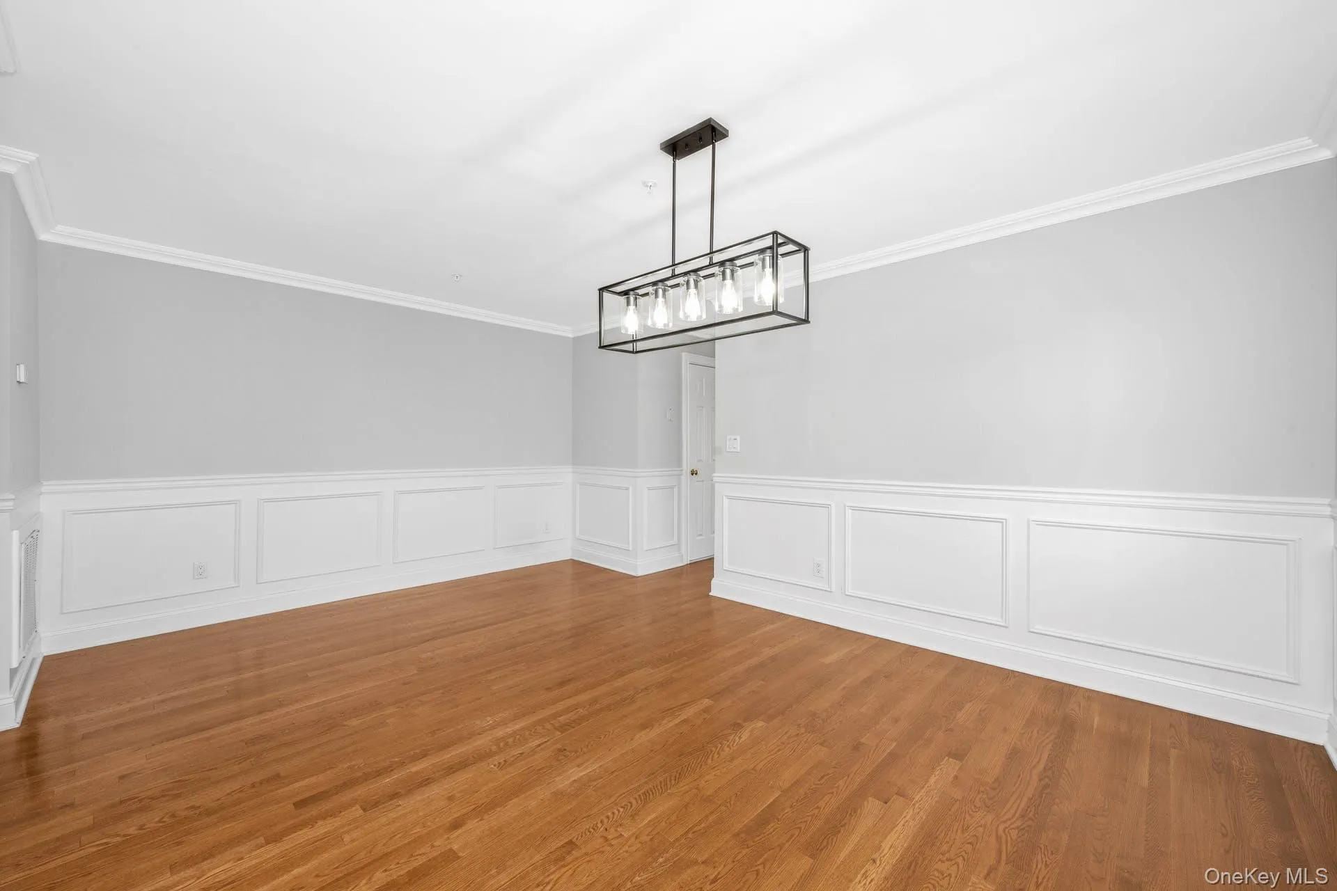 Unfurnished dining area featuring crown molding, a wainscoted wall, and wood finished floors Unfurnished dining area featuring crown molding, a wainscoted wall, and wood finished floors