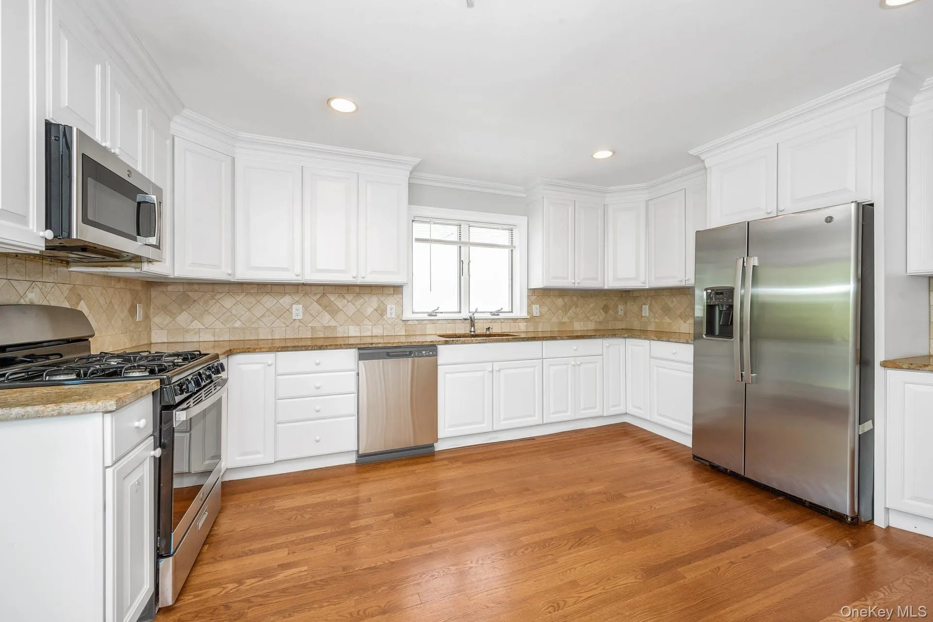 Kitchen with appliances with stainless steel finishes, light wood finished floors, white cabinetry, decorative backsplash, and recessed lighting Kitchen with appliances with stainless steel finishes, light wood finished floors, white cabinetry, decorative backsplash, and recessed lighting