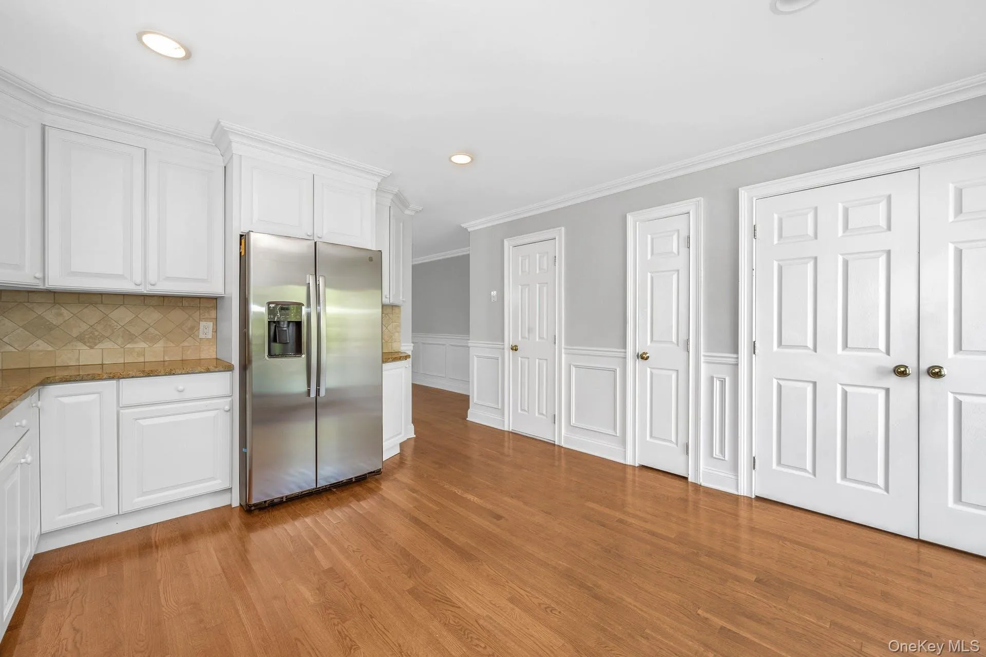 Kitchen featuring stainless steel fridge with ice dispenser, white cabinets, light wood finished floors, ornamental molding, and recessed lighting Kitchen featuring stainless steel fridge with ice dispenser, white cabinets, light wood finished floors, ornamental molding, and recessed lighting