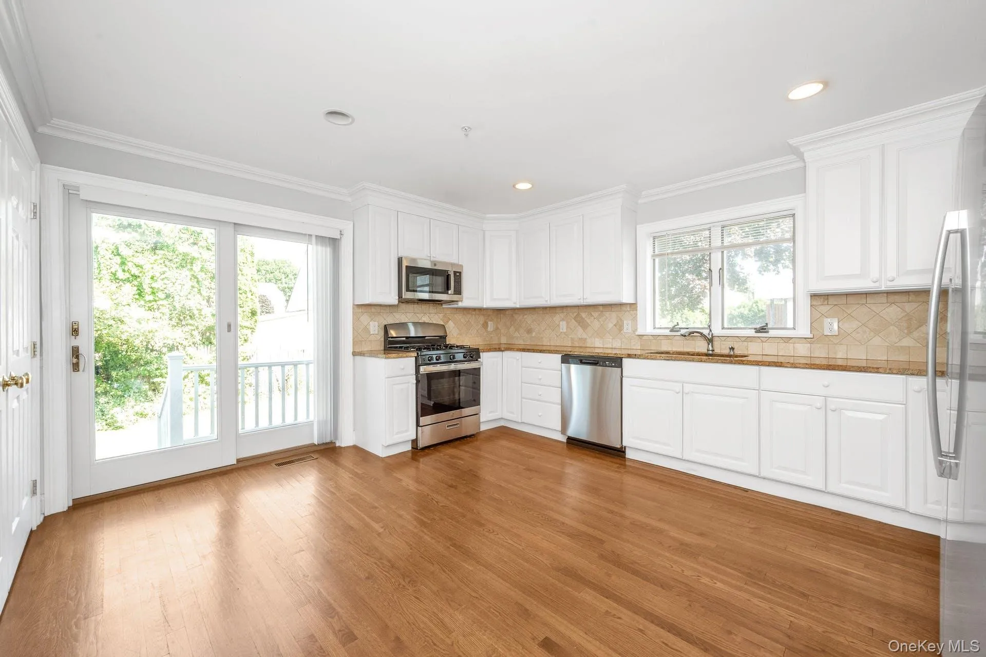 Kitchen featuring appliances with stainless steel finishes, light wood-style flooring, white cabinetry, ornamental molding, and recessed lighting Kitchen featuring appliances with stainless steel finishes, light wood-style flooring, white cabinetry, ornamental molding, and recessed lighting
