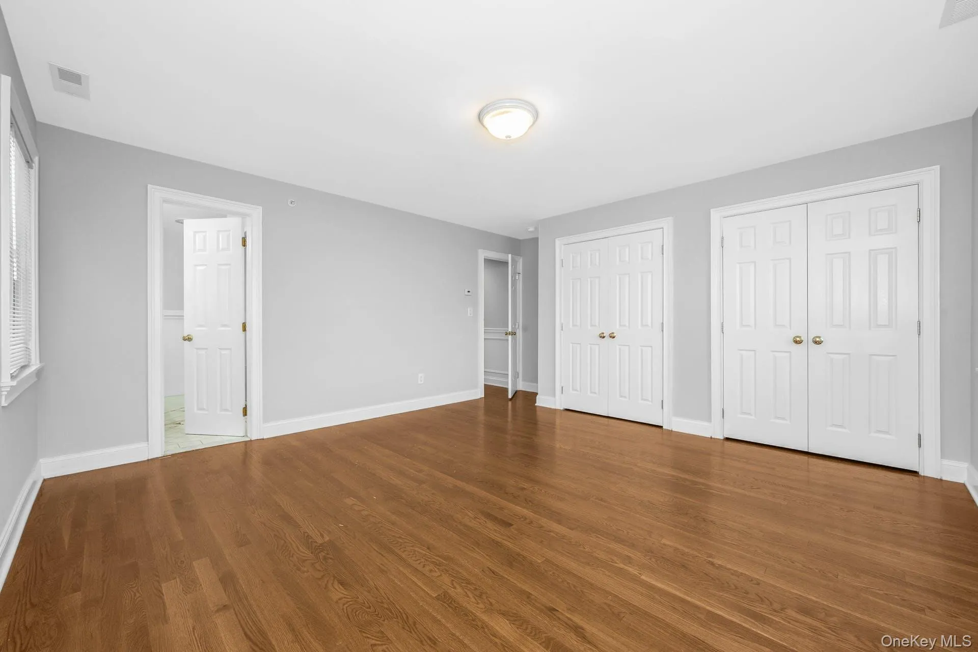 Unfurnished bedroom with multiple closets, wood finished floors, and connected bathroom Unfurnished bedroom with multiple closets, wood finished floors, and connected bathroom