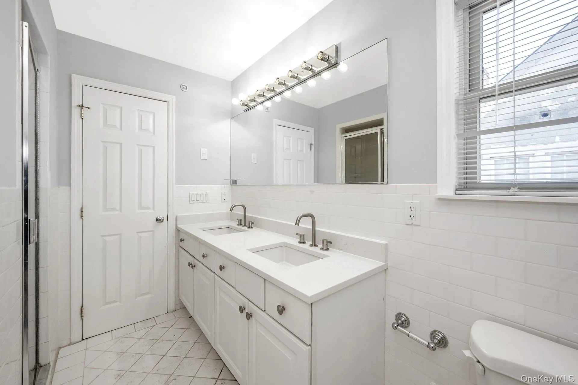 Bathroom with tile walls, double vanity, a wainscoted wall, and tile patterned flooring Bathroom with tile walls, double vanity, a wainscoted wall, and tile patterned flooring
