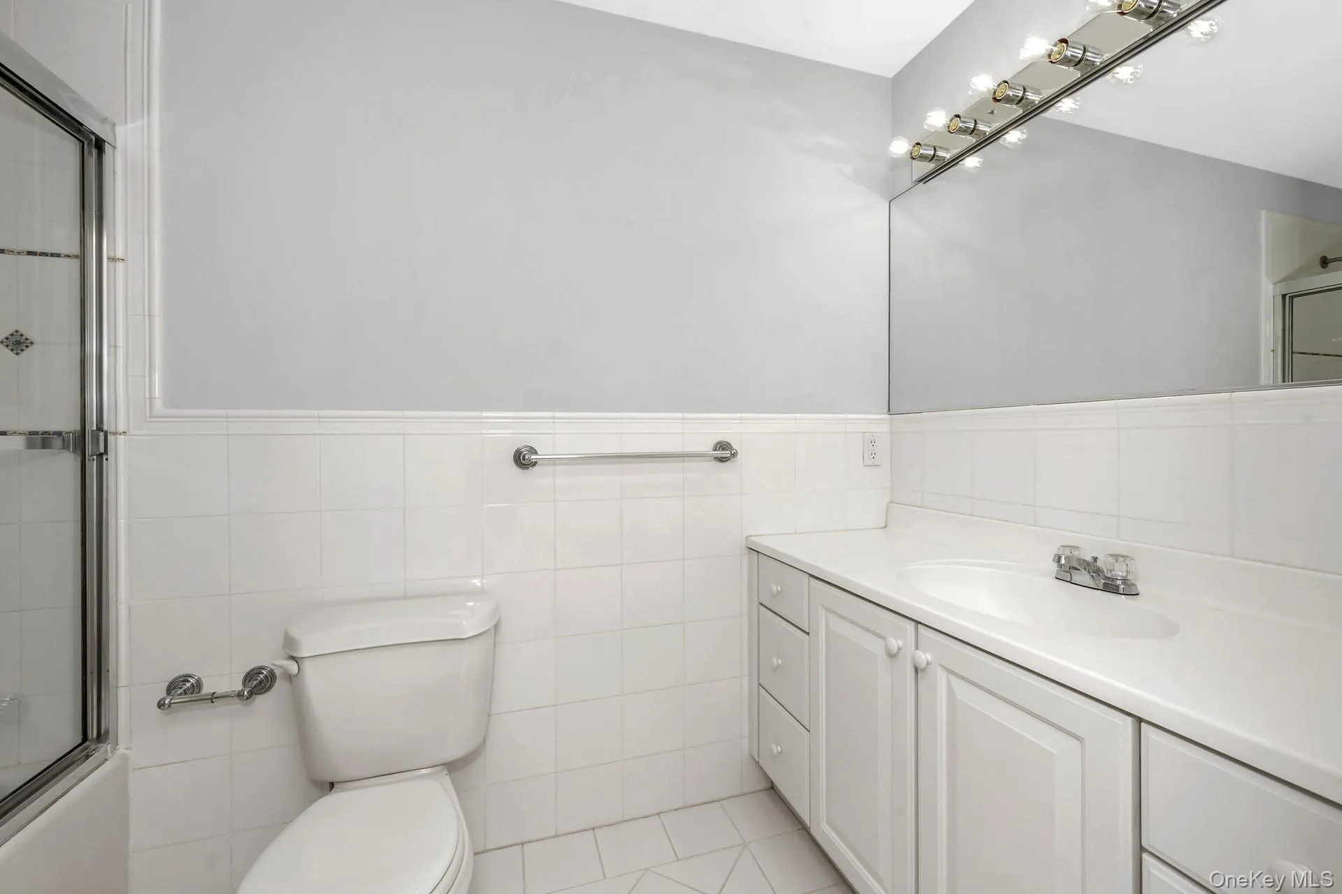 Full bath featuring vanity, tile walls, wainscoting, and combined bath / shower with glass door Full bath featuring vanity, tile walls, wainscoting, and combined bath / shower with glass door