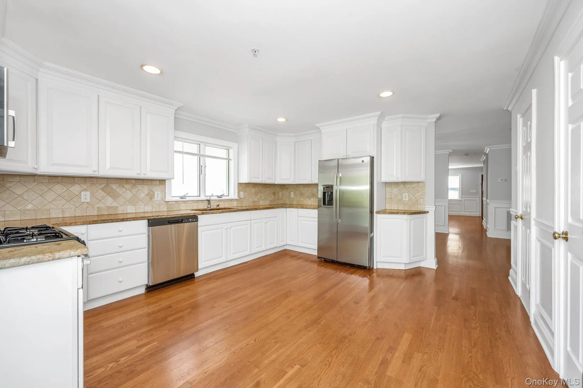 Kitchen featuring stainless steel appliances, light wood-style flooring, white cabinets, backsplash, and crown molding Kitchen featuring stainless steel appliances, light wood-style flooring, white cabinets, backsplash, and crown molding