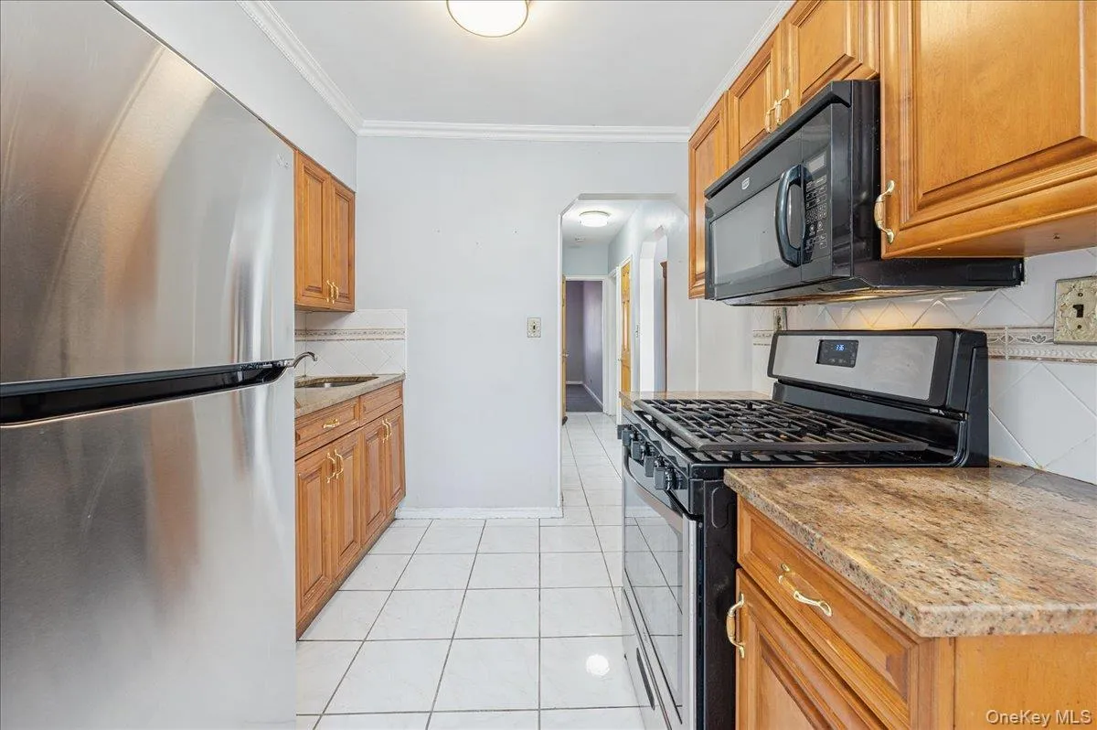 Kitchen with stainless steel appliances, light tile patterned floors, crown molding, light stone counters, and decorative backsplash Kitchen with stainless steel appliances, light tile patterned floors, crown molding, light stone counters, and decorative backsplash