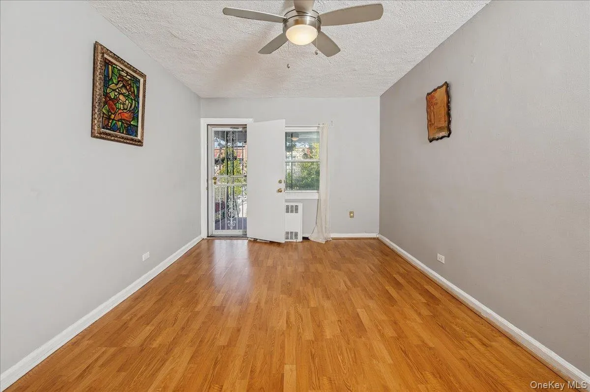 Primary bedroom with a textured ceiling, light finished floors, ceiling fan, and radiator heating unit; door leading out to balcony Primary bedroom with a textured ceiling, light finished floors, ceiling fan, and radiator heating unit; door leading out to balcony