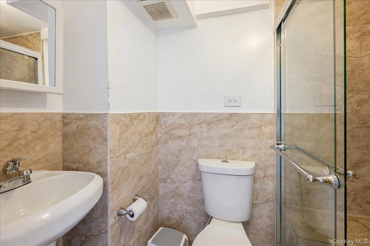 Full second bath featuring a shower stall, a wainscoted wall, and tile walls Full second bath featuring a shower stall, a wainscoted wall, and tile walls