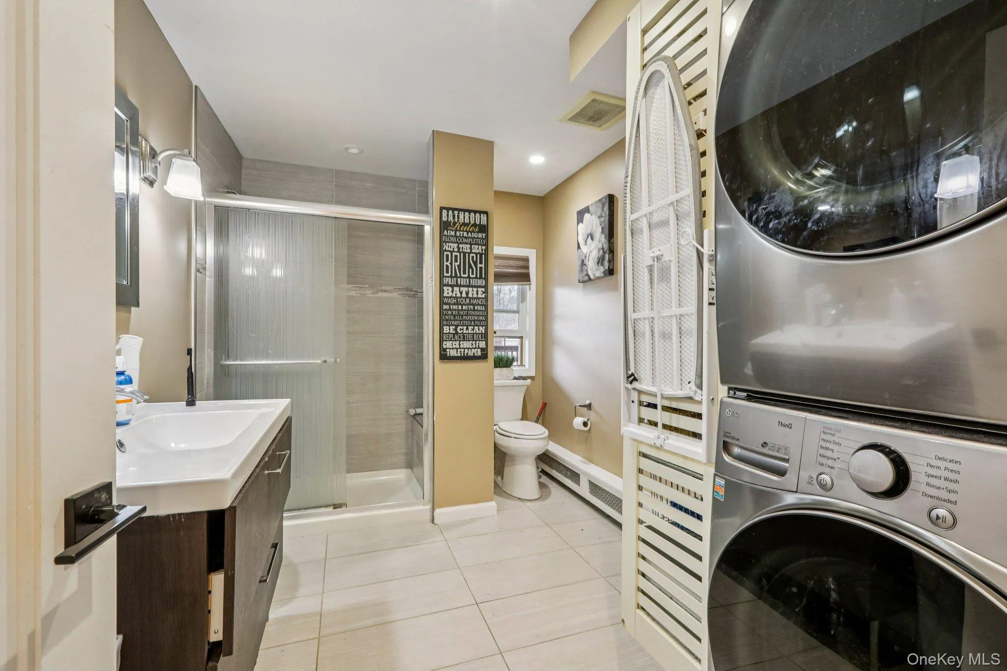 Bathroom featuring vanity, light tile patterned floors, a shower stall, and stacked washing machine and dryer Bathroom featuring vanity, light tile patterned floors, a shower stall, and stacked washing machine and dryer