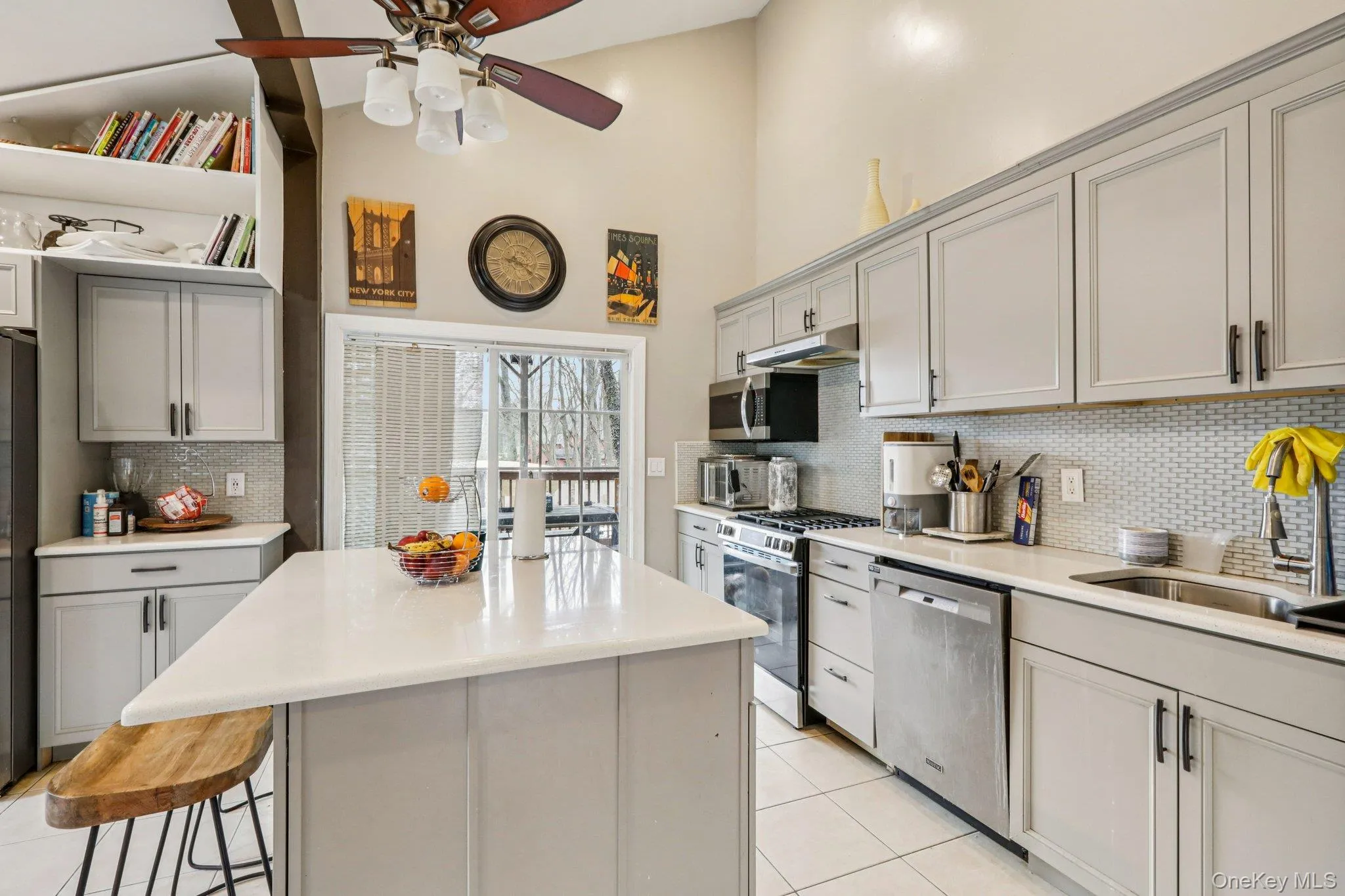 Kitchen featuring gray cabinetry, stainless steel appliances, a kitchen island, a ceiling fan, and a high ceiling Kitchen featuring gray cabinetry, stainless steel appliances, a kitchen island, a ceiling fan, and a high ceiling