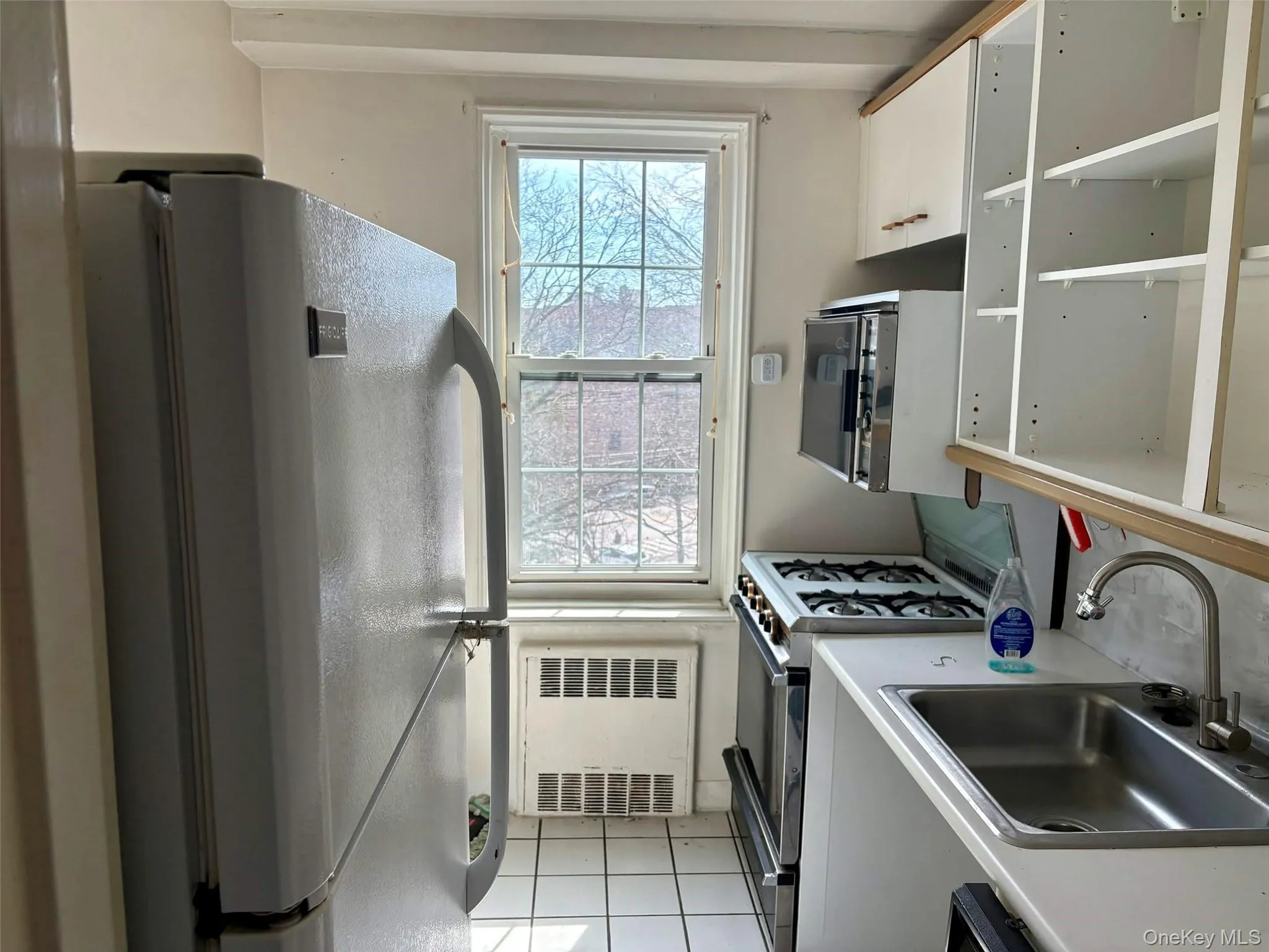 Kitchen featuring freestanding refrigerator, white cabinets, light countertops, radiator, and light tile patterned floors Kitchen featuring freestanding refrigerator, white cabinets, light countertops, radiator, and light tile patterned floors