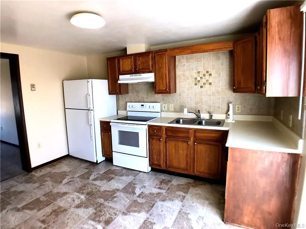 Kitchen featuring white appliances, light countertops, wood finish cabinetry, stone finish floors, and tasteful backsplash Kitchen featuring white appliances, light countertops, wood finish cabinetry, stone finish floors, and tasteful backsplash