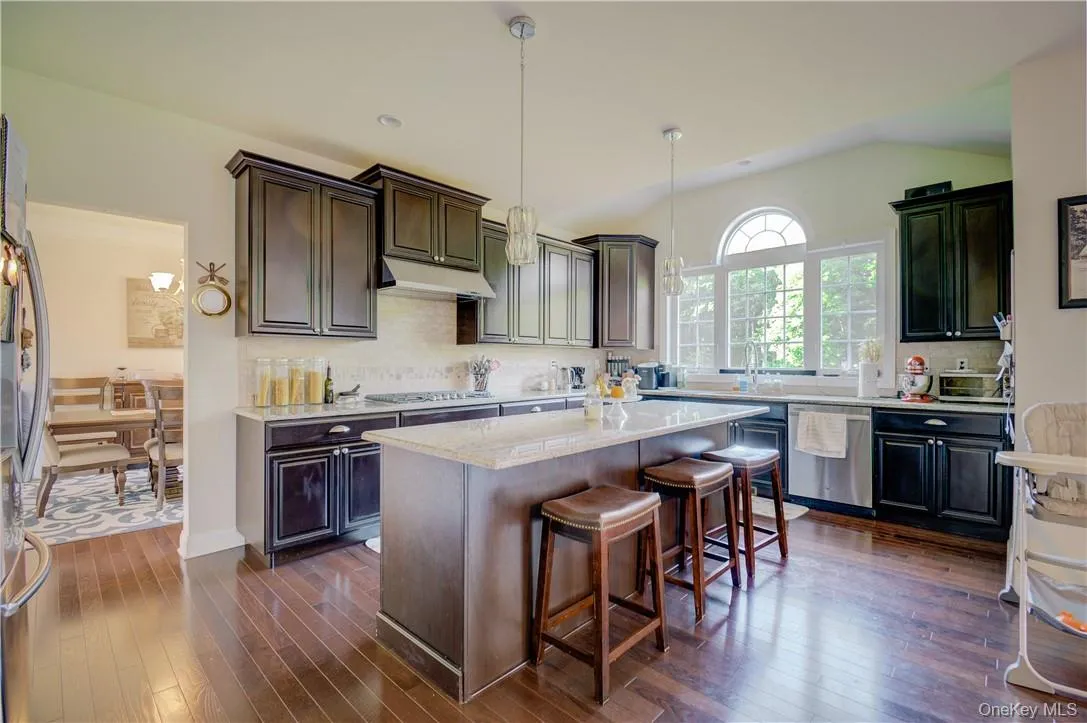 Kitchen featuring stainless steel appliances, vaulted ceiling, decorative light fixtures, dark wood-type flooring, and a kitchen island Kitchen featuring stainless steel appliances, vaulted ceiling, decorative light fixtures, dark wood-type flooring, and a kitchen island
