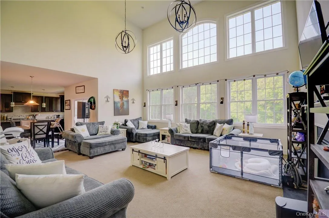 Carpeted living room featuring a high ceiling and a notable chandelier Carpeted living room featuring a high ceiling and a notable chandelier