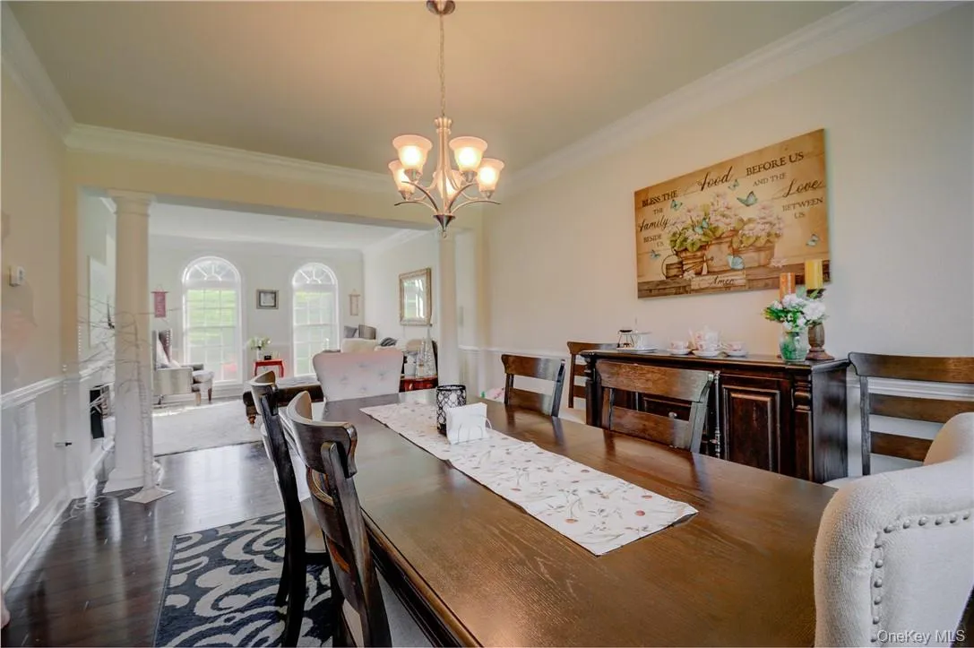 Dining room featuring a notable chandelier, ornamental molding, decorative columns, and dark wood-type flooring Dining room featuring a notable chandelier, ornamental molding, decorative columns, and dark wood-type flooring
