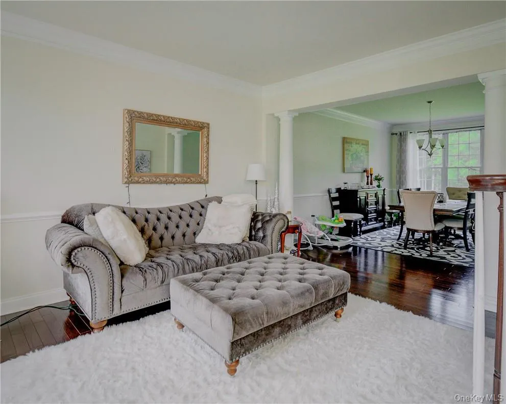 Living room with a notable chandelier, ornamental molding, ornate columns, and wood-type flooring Living room with a notable chandelier, ornamental molding, ornate columns, and wood-type flooring