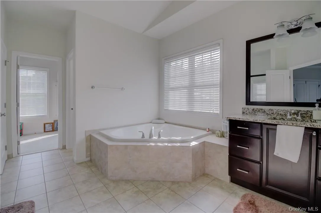 Master Bathroom featuring a relaxing tiled bath, vaulted ceiling, vanity, and tile floors Master Bathroom featuring a relaxing tiled bath, vaulted ceiling, vanity, and tile floors