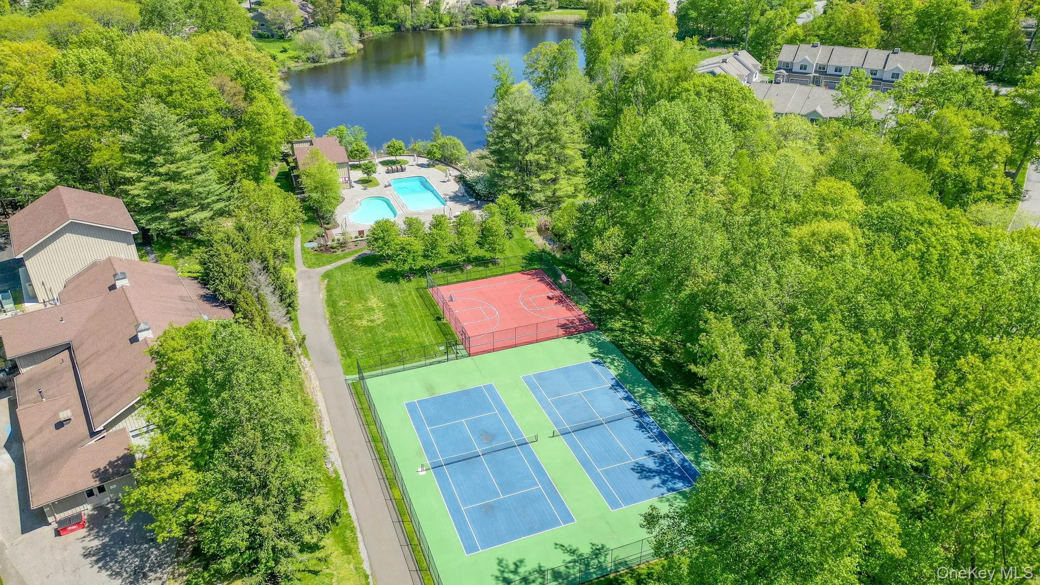 Drone view of the clubhouse, tennis and basketball courts and pond Drone view of the clubhouse, tennis and basketball courts and pond