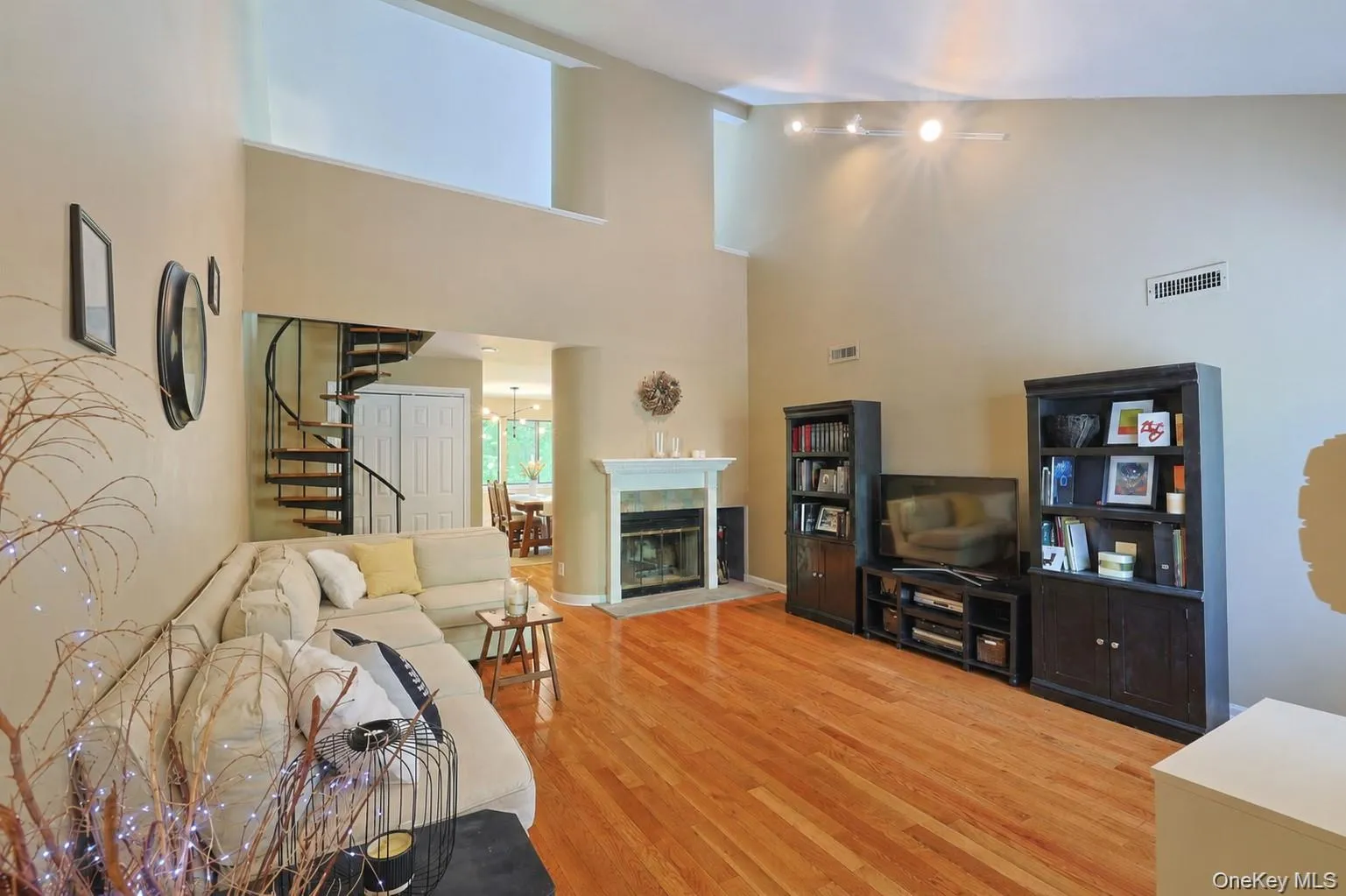 Two-story living area featuring hardwood flooring, a white mantel fireplace, and high ceilings Two-story living area featuring hardwood flooring, a white mantel fireplace, and high ceilings