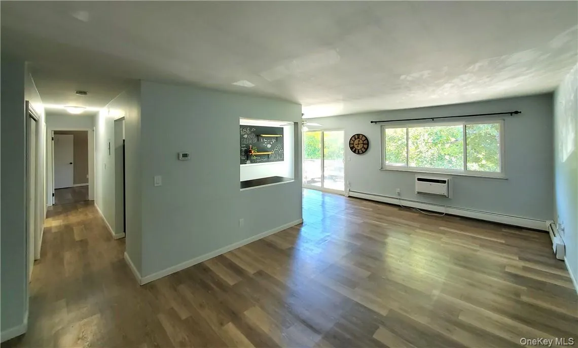 Living room featuring dark wood-type flooring, a baseboard radiator, and a wall mounted air conditioner Living room featuring dark wood-type flooring, a baseboard radiator, and a wall mounted air conditioner