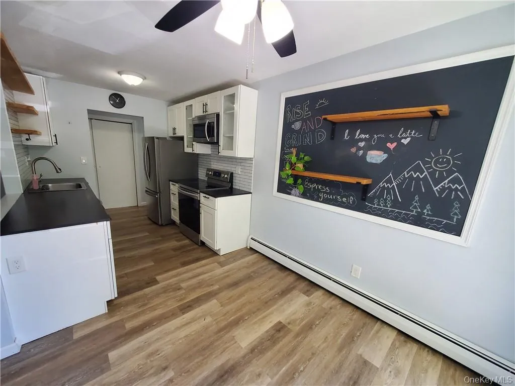 Kitchen with hardwood / wood-style floors, tasteful backsplash, stainless steel appliances, sink, and white cabinetry Kitchen with hardwood / wood-style floors, tasteful backsplash, stainless steel appliances, sink, and white cabinetry