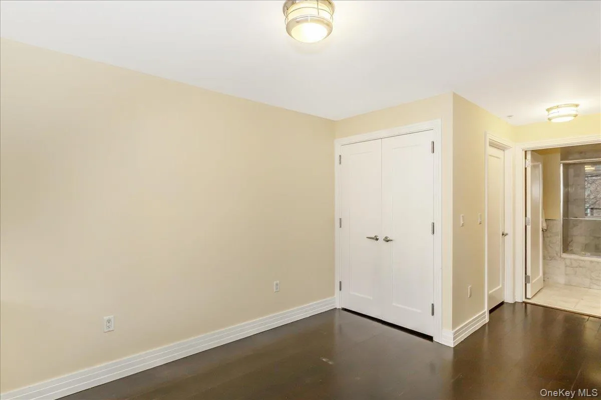Unfurnished bedroom with dark wood-style flooring, a closet, and ensuite bath Unfurnished bedroom with dark wood-style flooring, a closet, and ensuite bath