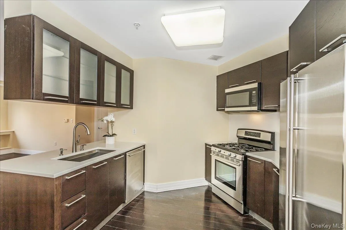 Kitchen featuring stainless steel appliances, glass insert cabinets, dark wood finished floors, and dark brown cabinets Kitchen featuring stainless steel appliances, glass insert cabinets, dark wood finished floors, and dark brown cabinets