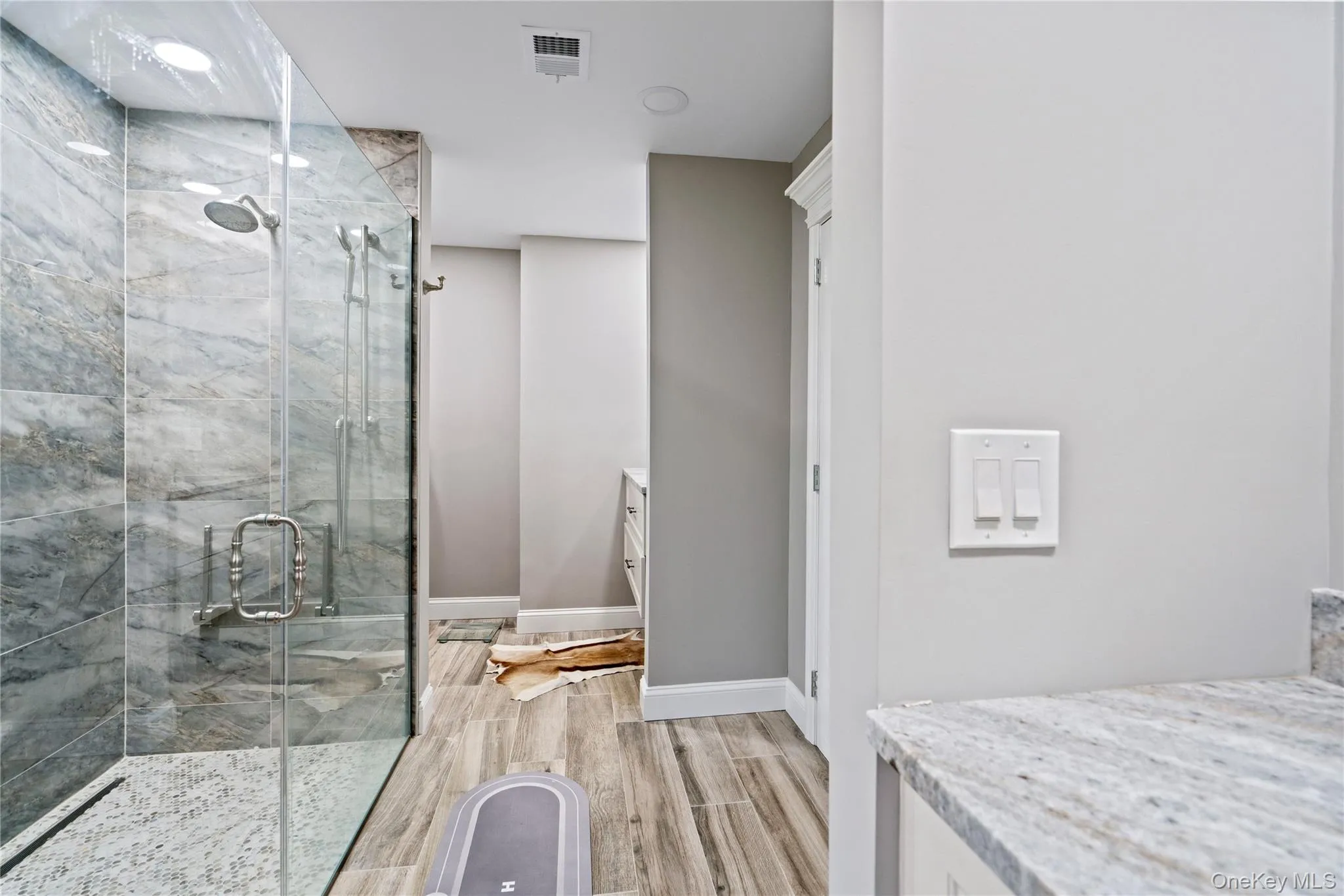 Full bathroom featuring vanity, a marble finish shower, and light wood-style flooring Full bathroom featuring vanity, a marble finish shower, and light wood-style flooring