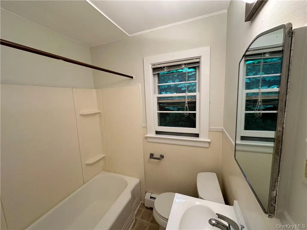 Bathroom with a baseboard radiator, tile walls, toilet, tile floors, and shower / bathtub combination Bathroom with a baseboard radiator, tile walls, toilet, tile floors, and shower / bathtub combination