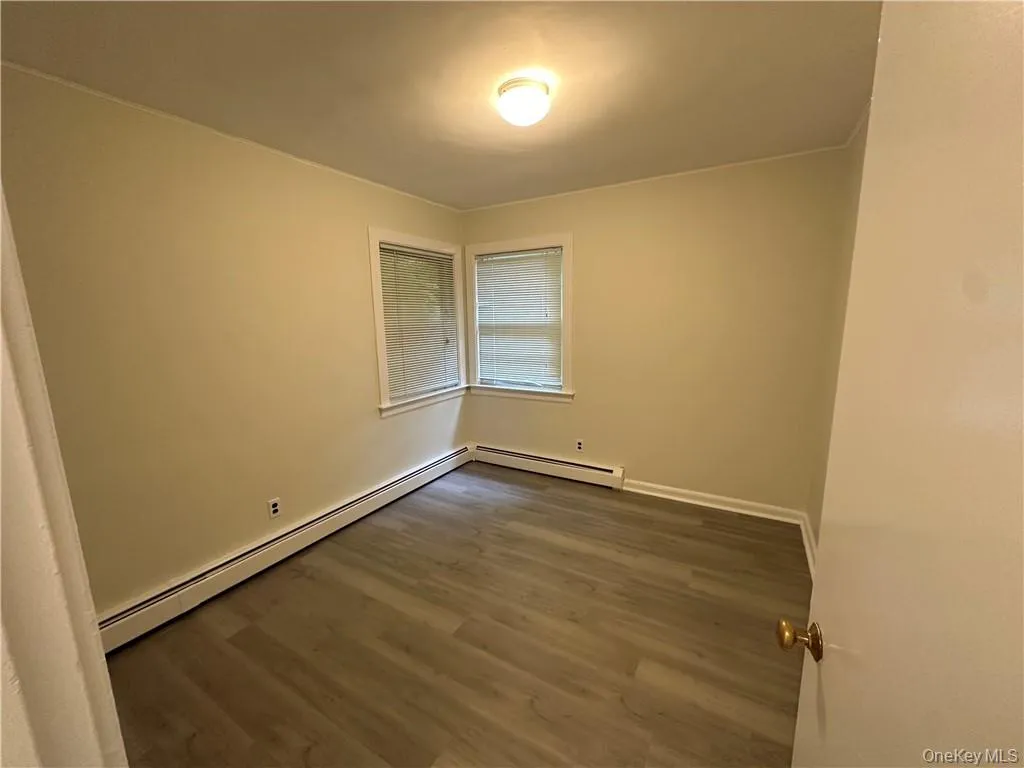 Empty room with a baseboard heating unit and dark hardwood / wood-style floors Empty room with a baseboard heating unit and dark hardwood / wood-style floors