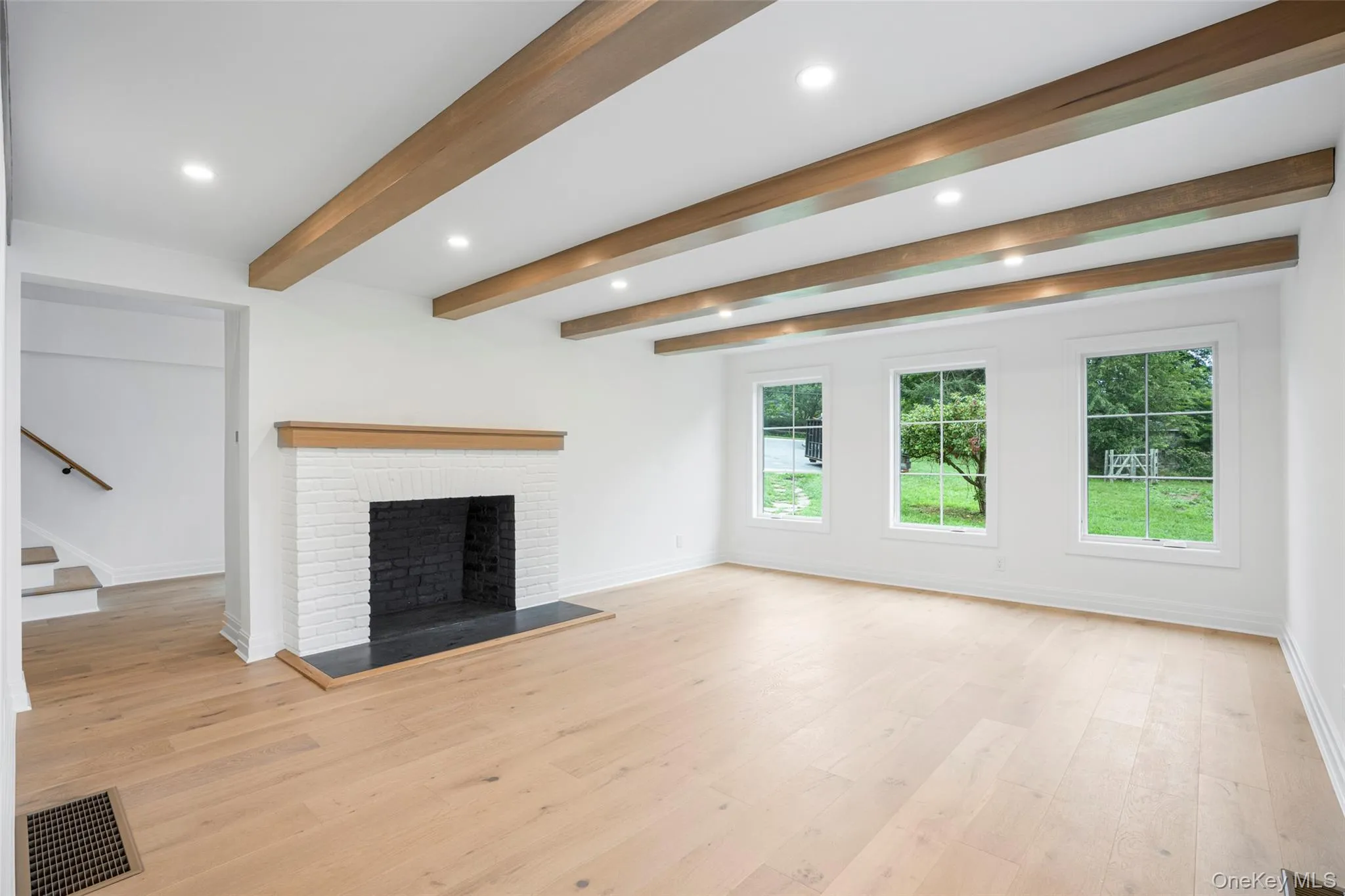 Unfurnished living room with recessed lighting, light wood finished floors, a brick fireplace, and beamed ceiling Unfurnished living room with recessed lighting, light wood finished floors, a brick fireplace, and beamed ceiling