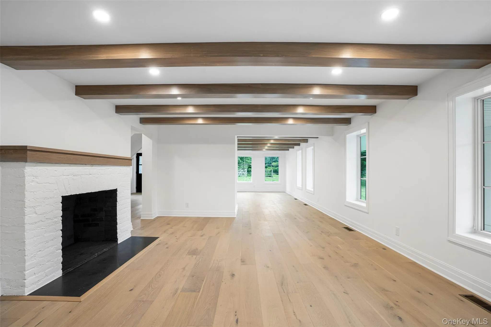 Unfurnished living room featuring a brick fireplace, beam ceiling, light wood-type flooring, and recessed lighting Unfurnished living room featuring a brick fireplace, beam ceiling, light wood-type flooring, and recessed lighting