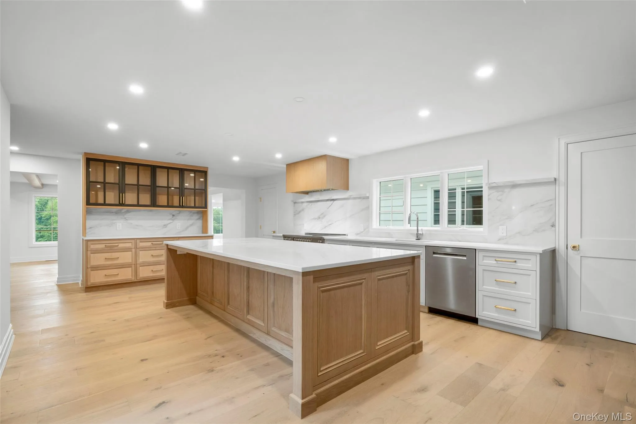 Custom built kitchen with dishwasher, quartz backsplash, a kitchen island, light countertops, and recessed lighting and fireplace. Access to side entrance and mudroom Custom built kitchen with dishwasher, quartz backsplash, a kitchen island, light countertops, and recessed lighting and fireplace. Access to side entrance and mudroom