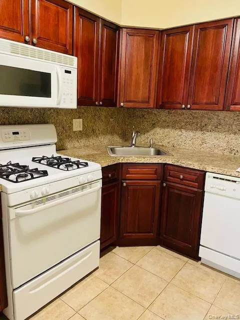 Kitchen featuring white appliances, reddish brown cabinets, light tile patterned flooring, and tasteful backsplash Kitchen featuring white appliances, reddish brown cabinets, light tile patterned flooring, and tasteful backsplash