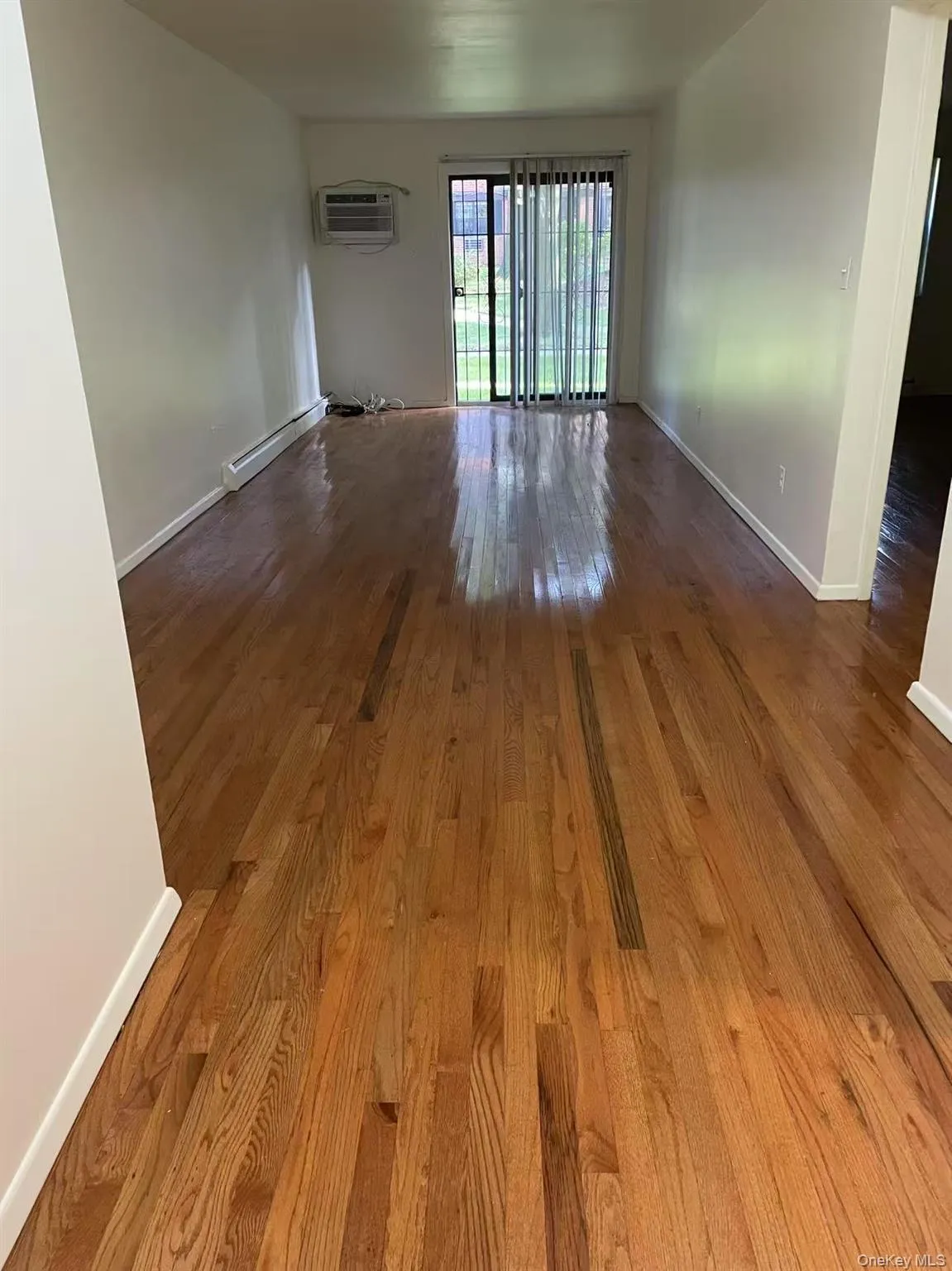 Spare room featuring wood finished floors, a wall mounted AC, and baseboard heating Spare room featuring wood finished floors, a wall mounted AC, and baseboard heating