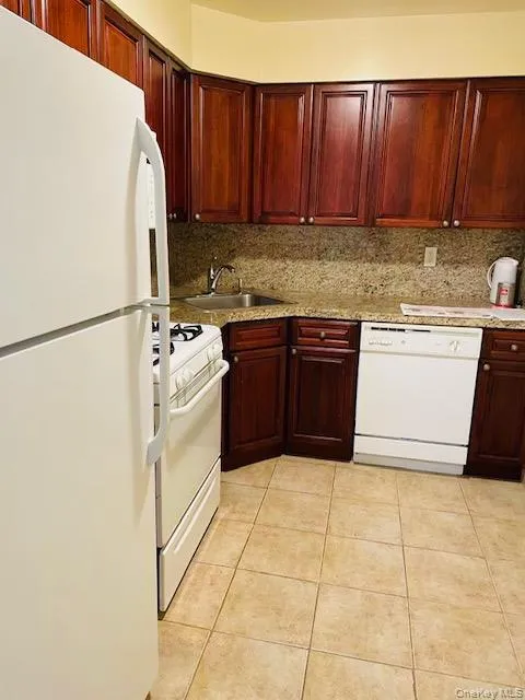 Kitchen featuring white appliances, backsplash, dark brown cabinets, and light tile patterned floors Kitchen featuring white appliances, backsplash, dark brown cabinets, and light tile patterned floors