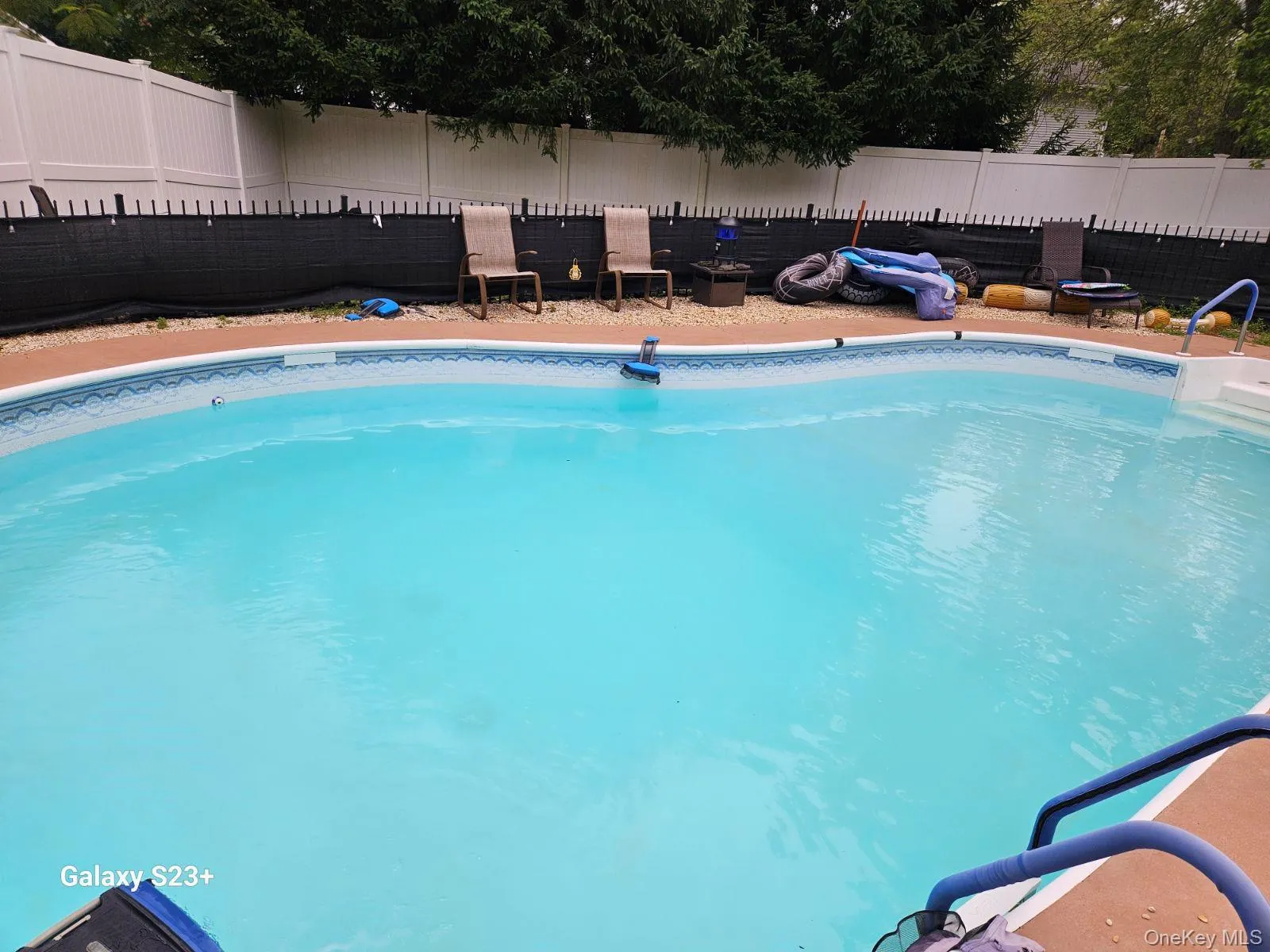 Inviting in-ground pool with integrated steps, surrounded by a painted concrete deck and a white privacy fence Inviting in-ground pool with integrated steps, surrounded by a painted concrete deck and a white privacy fence