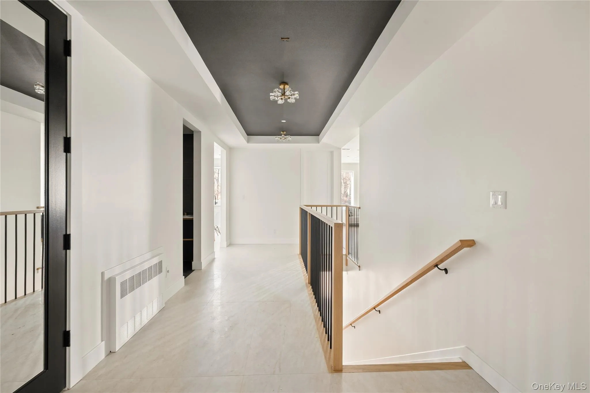 Corridor with an upstairs landing, radiator heating unit, a raised ceiling, and a chandelier Corridor with an upstairs landing, radiator heating unit, a raised ceiling, and a chandelier
