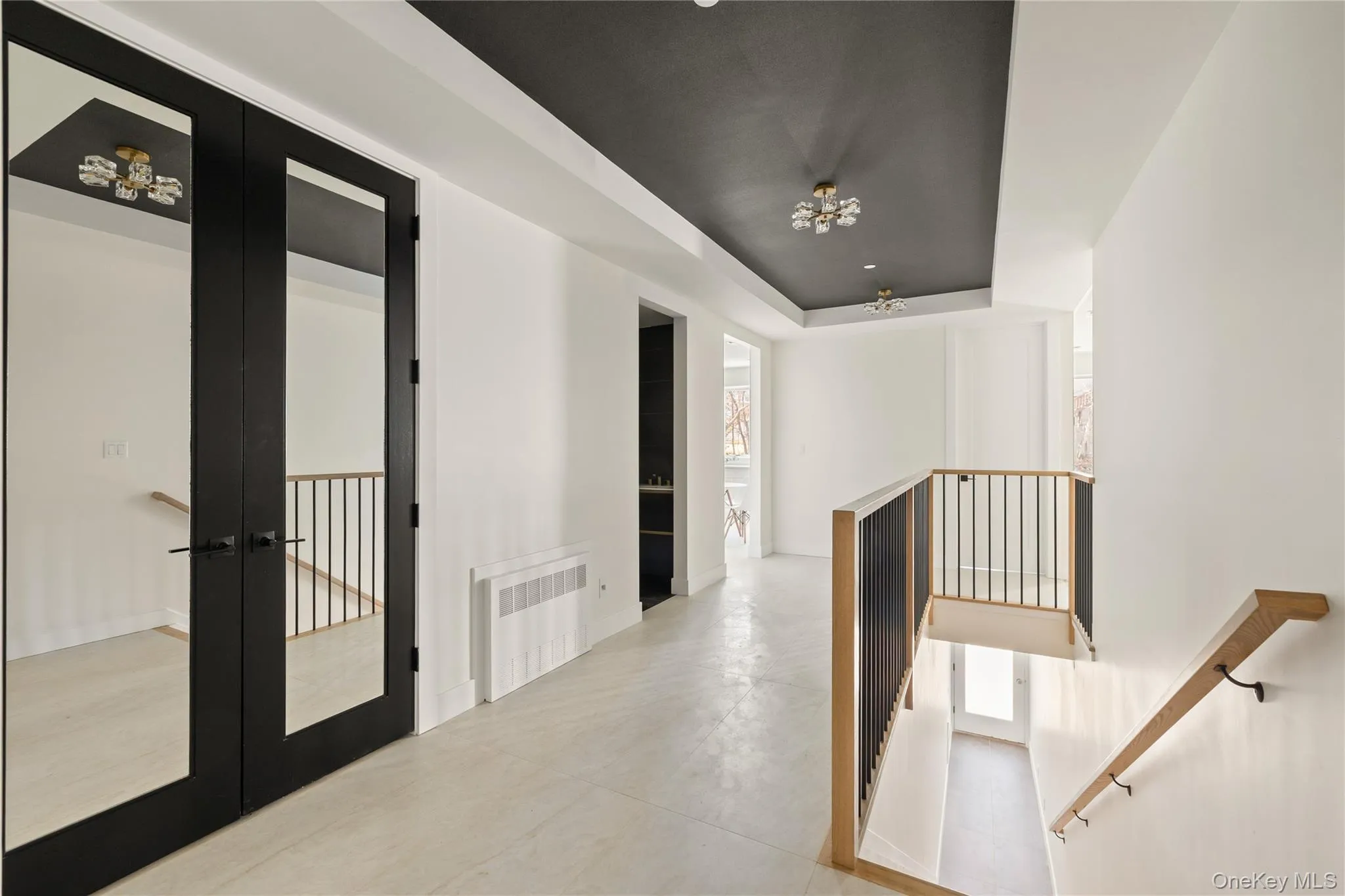 Hallway featuring a tray ceiling, french doors, radiator heating unit, and an upstairs landing Hallway featuring a tray ceiling, french doors, radiator heating unit, and an upstairs landing