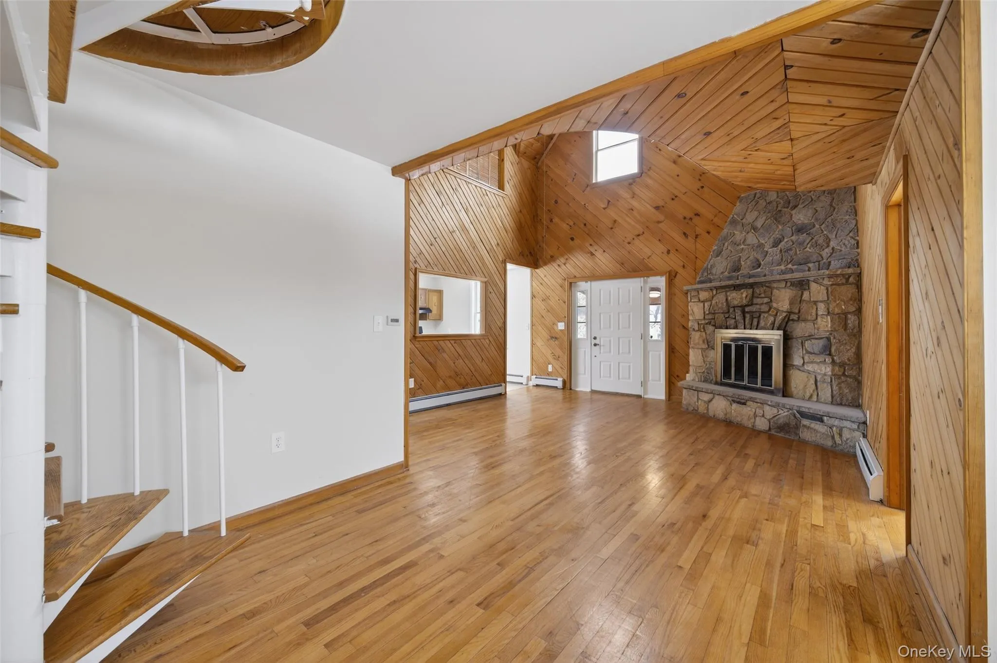 Unfurnished living room with wooden walls, a stone fireplace, light wood-style floors, a baseboard radiator, and baseboard heating Unfurnished living room with wooden walls, a stone fireplace, light wood-style floors, a baseboard radiator, and baseboard heating