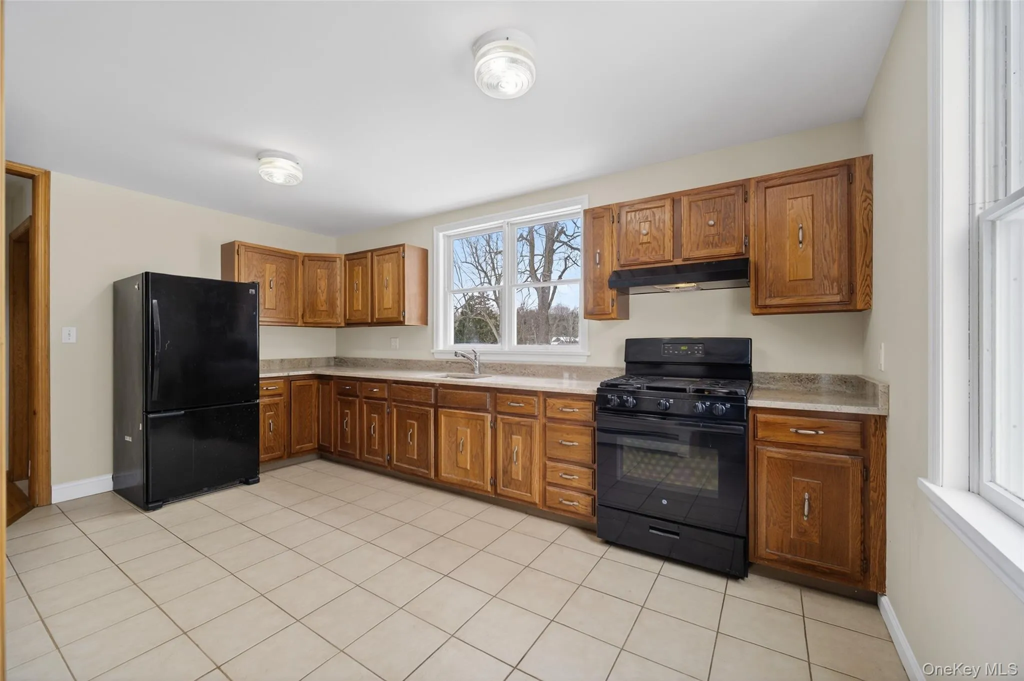 Kitchen featuring black appliances, wood finish cabinetry, and light tile patterned floors Kitchen featuring black appliances, wood finish cabinetry, and light tile patterned floors