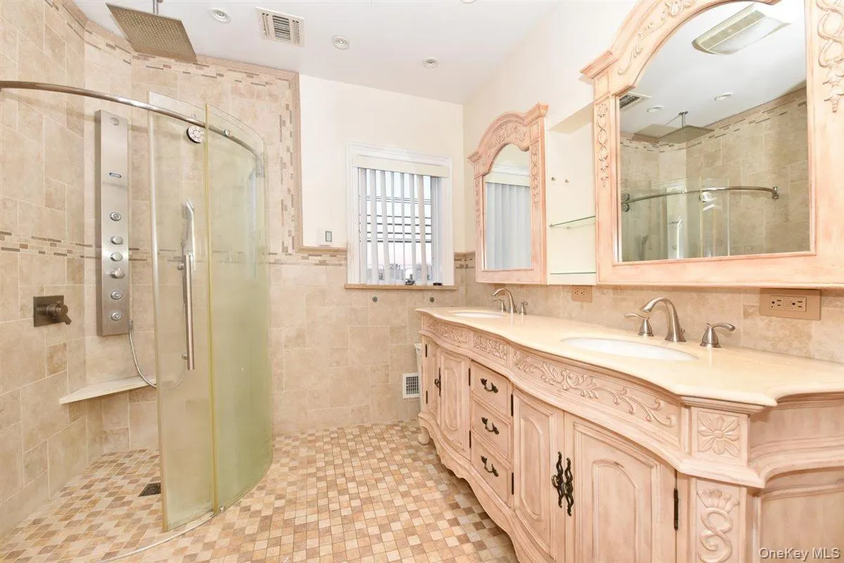 Full bathroom featuring double vanity, a stall shower, tile walls, and wainscoting Full bathroom featuring double vanity, a stall shower, tile walls, and wainscoting