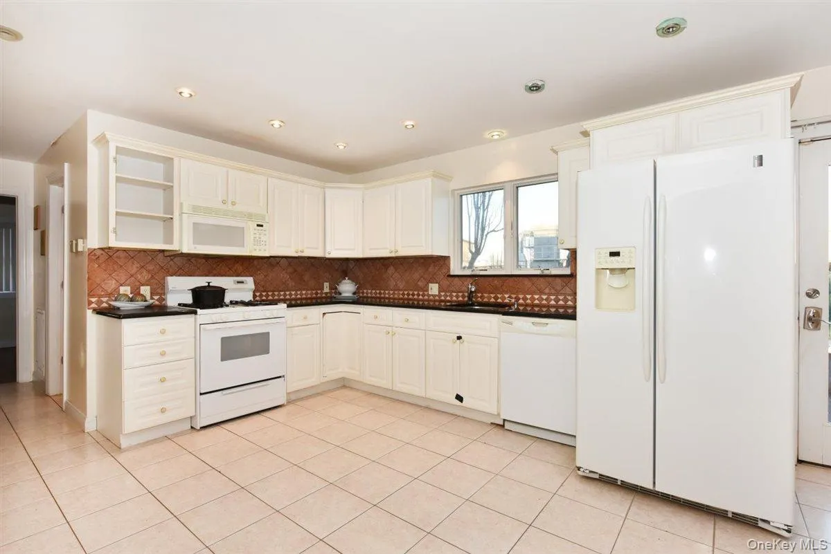 Kitchen with white appliances, open shelves, dark countertops, light tile patterned floors, and white cabinetry Kitchen with white appliances, open shelves, dark countertops, light tile patterned floors, and white cabinetry
