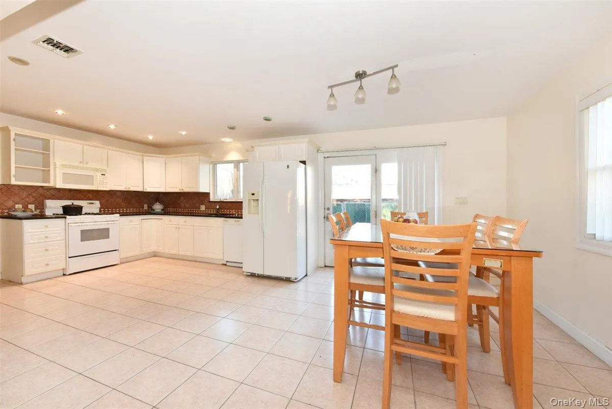 Kitchen featuring white appliances, dark countertops, white cabinetry, glass insert cabinets, and light tile patterned floors Kitchen featuring white appliances, dark countertops, white cabinetry, glass insert cabinets, and light tile patterned floors