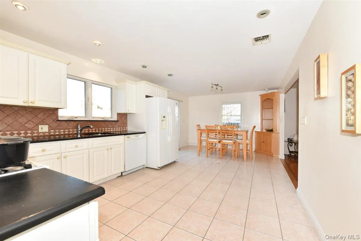 Kitchen featuring dark countertops, white appliances, white cabinetry, and light tile patterned floors Kitchen featuring dark countertops, white appliances, white cabinetry, and light tile patterned floors