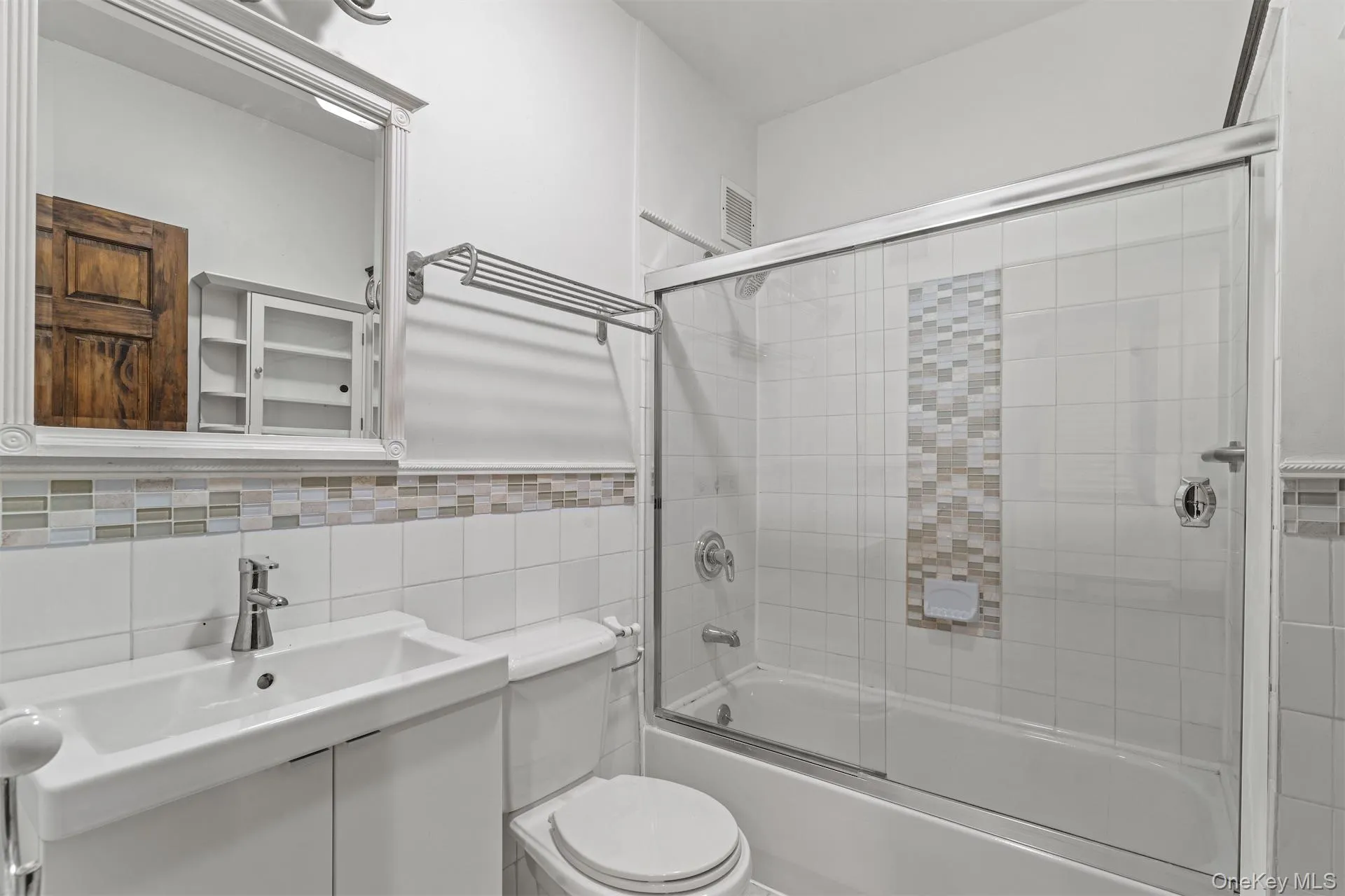 Bathroom featuring vanity, combined bath / shower with glass door, tile walls, and a wainscoted wall Bathroom featuring vanity, combined bath / shower with glass door, tile walls, and a wainscoted wall
